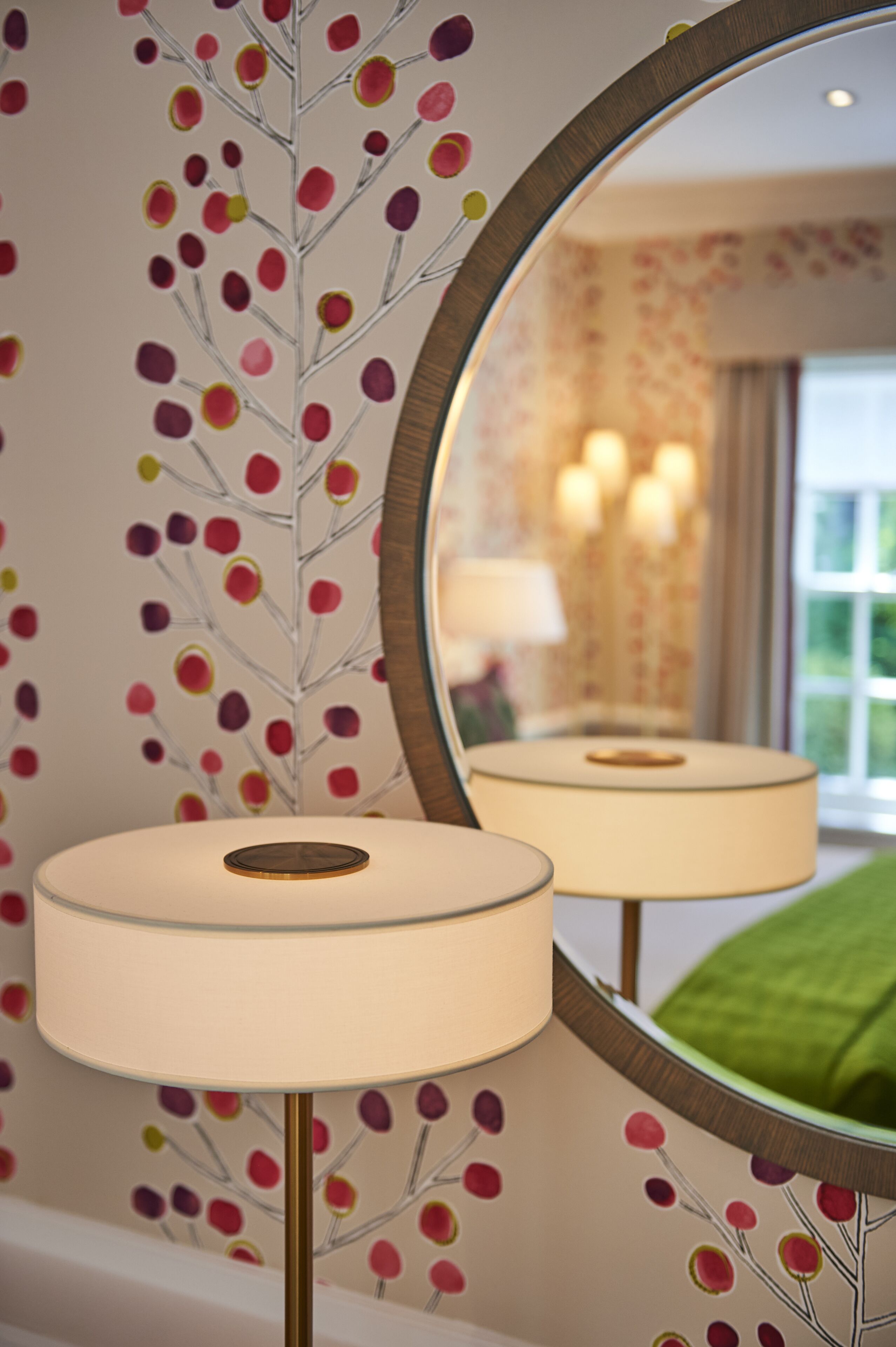 Une pièce avec un miroir qui reflète une lampe et un mur orné d’un motif à pois.