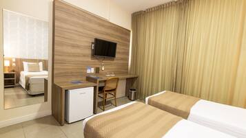 A hotel room with a bed, a desk with a computer, a TV, and a small fridge.