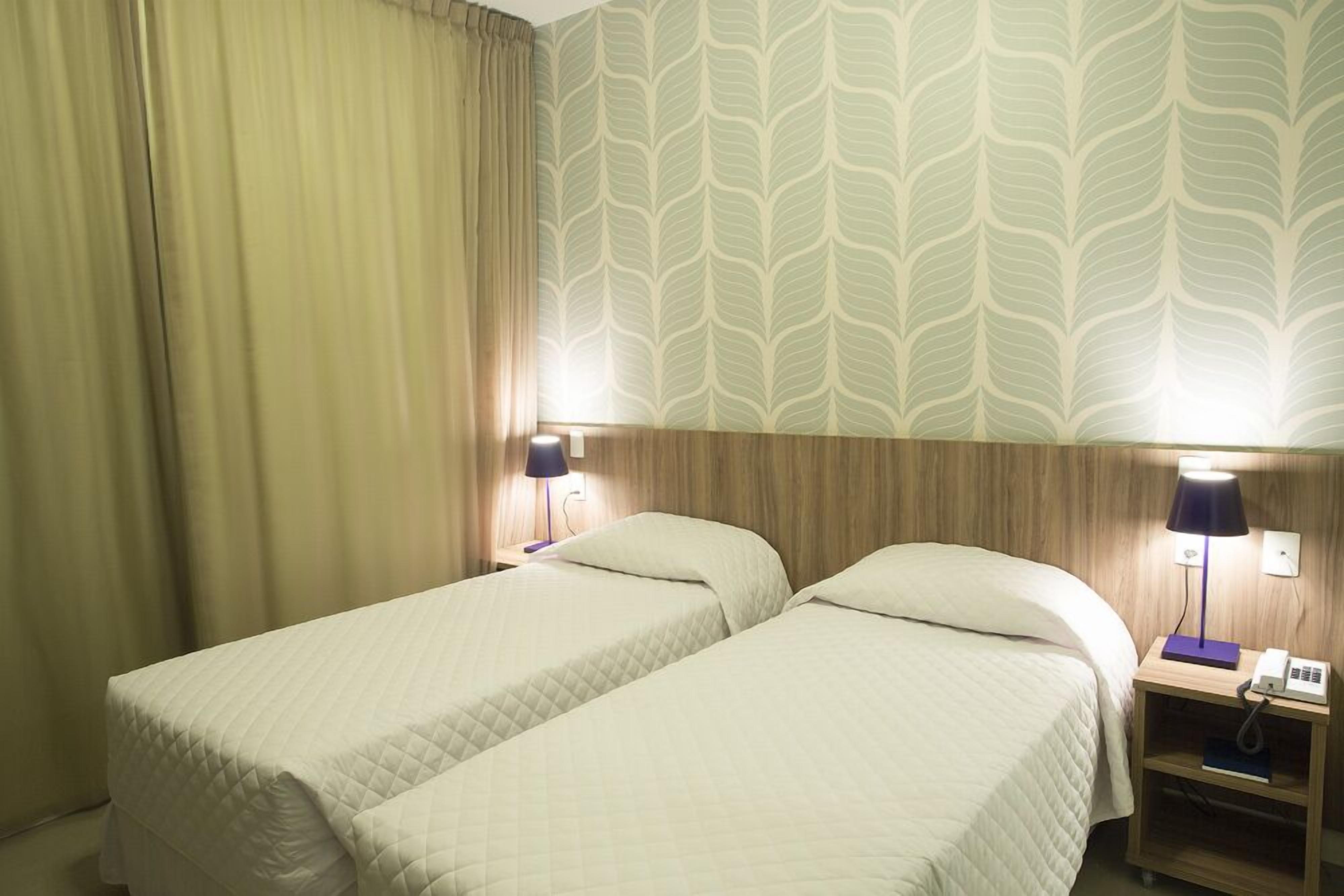 A hotel room with two beds, a wooden headboard, a nightstand with a lamp, and a telephone.