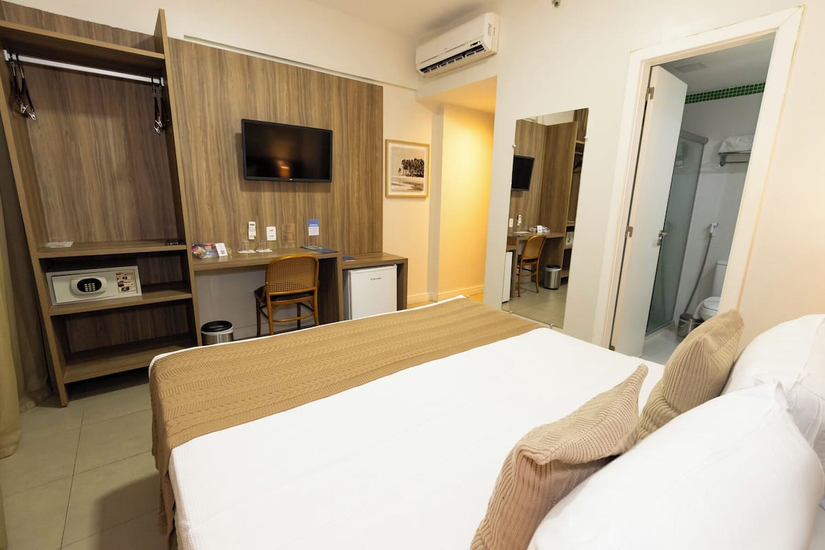 A hotel room with a bed, a desk, a chair, a television, and a wardrobe.