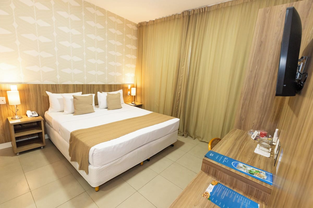 A hotel room with a large bed, two bedside tables with lamps, a TV mounted on the wall, and a wooden desk with a menu.