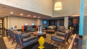 A lobby with multiple seating areas, a reception desk, and a television screen. - Mais Hotel Aeroporto Salvador (Lauro de Freitas)
