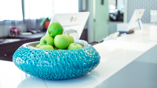 A blue bowl with green apples on a white table in a modern office setting.