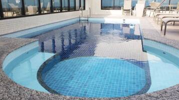 Piscina interior com água azul cristalina, rodeada por um deck com pedras e espreguiçadeiras.