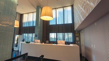A reception area with a counter, a large window with curtains, a hanging lamp, and a tiled wall.