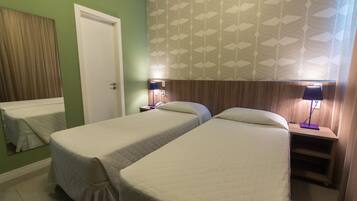 A hotel room with two single beds, a wooden headboard, a nightstand with a lamp, and a green wall.