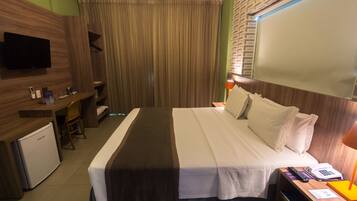 A hotel room with a bed, a desk, a television, and a small refrigerator.