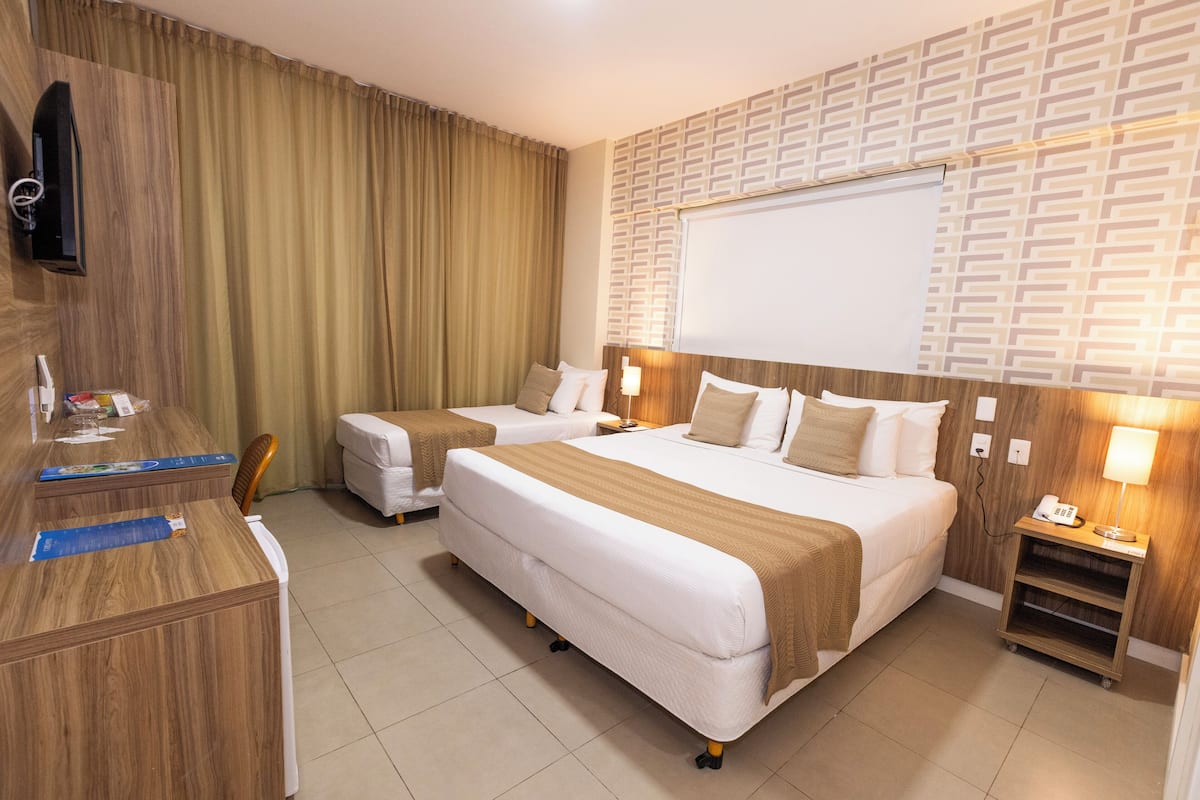 A hotel room with two beds, a desk, a TV, and a patterned wall.