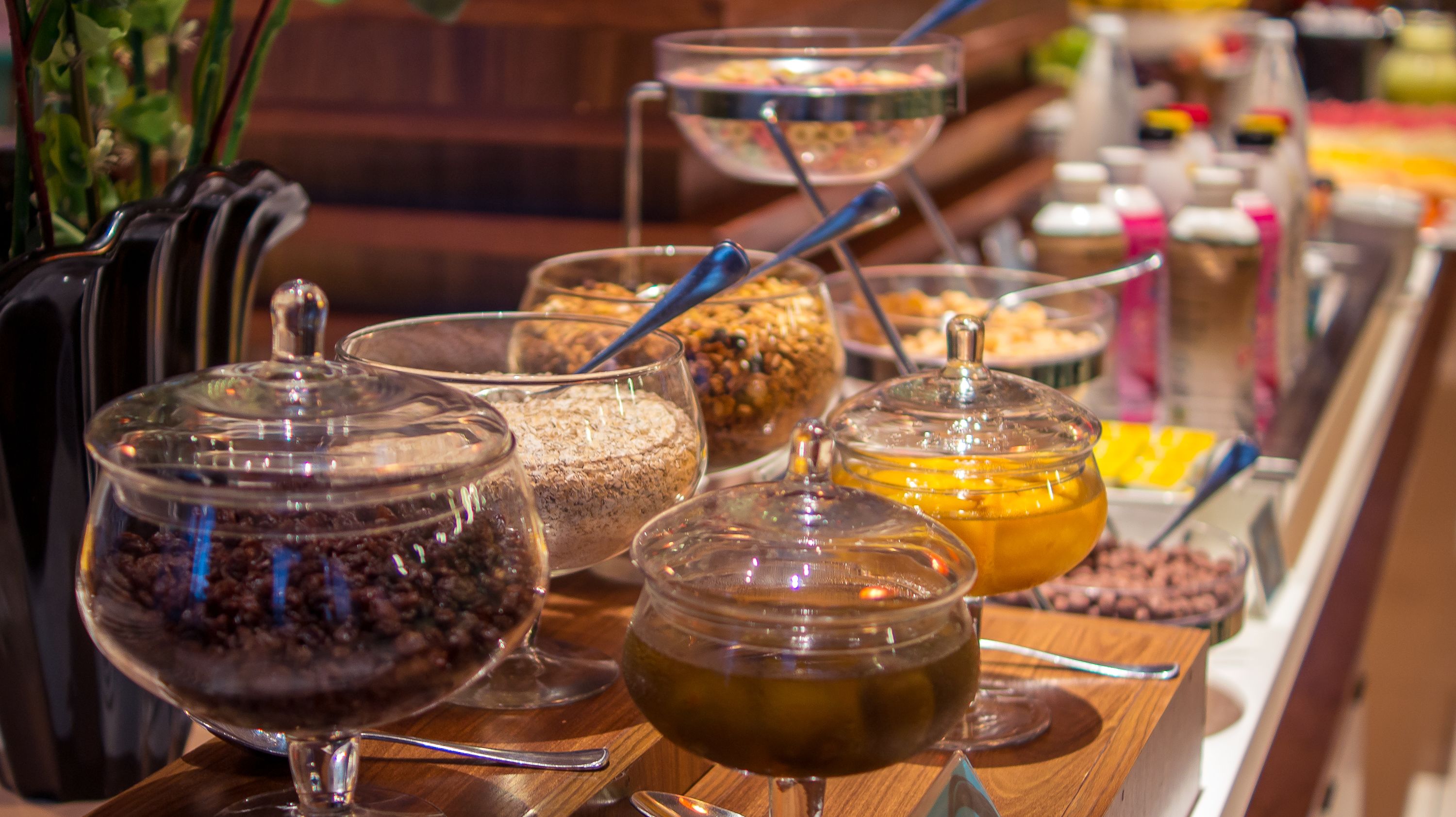 Un bufé con diversos alimentos en recipientes transparentes, que parecen frutos secos, frutas deshidratadas y posiblemente un postre.