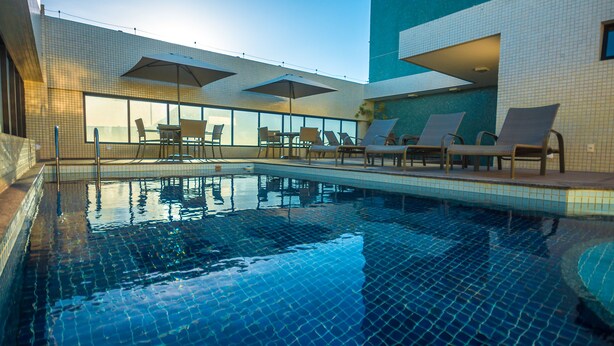 An indoor swimming pool with tiled walls, lounge chairs, and umbrellas. - Mais Hotel Aeroporto Salvador (Lauro de Freitas)
