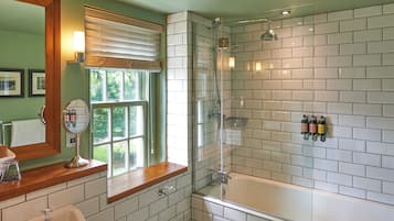 A bathroom with a glass-enclosed shower, a vanity with a mirror, and a window with blinds.
