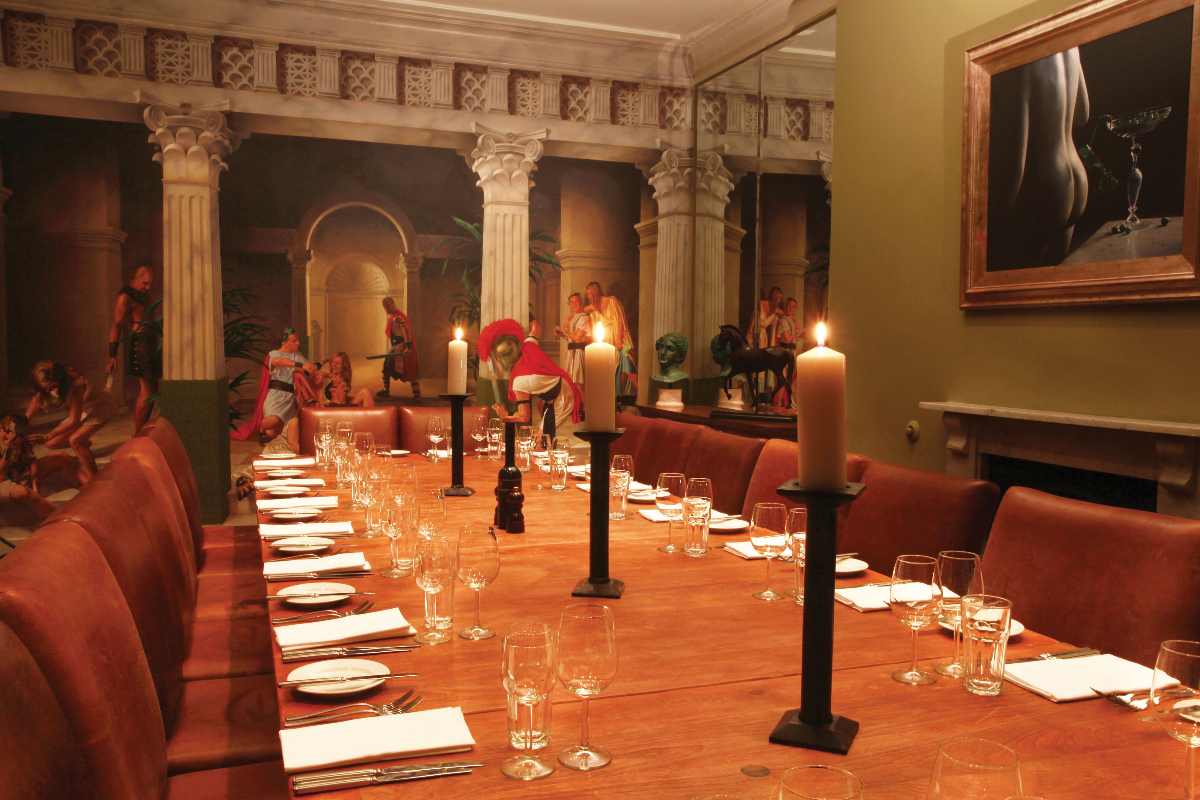 A long dining table set for a meal in a restaurant with red leather booths and a classical architectural backdrop.