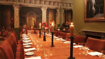 A long dining table set for a meal in a restaurant with red leather booths and a classical architectural backdrop.