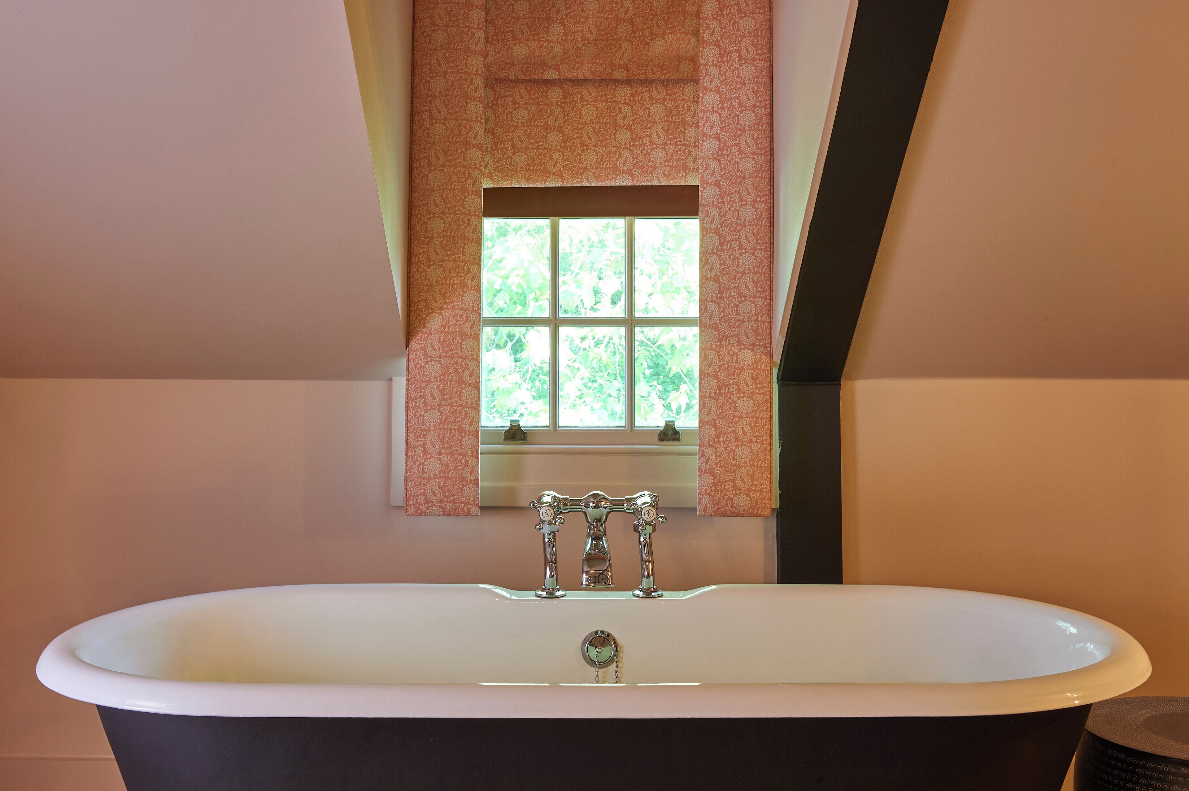 A bathroom with a freestanding bathtub, a window with a view of greenery, and a patterned wall.