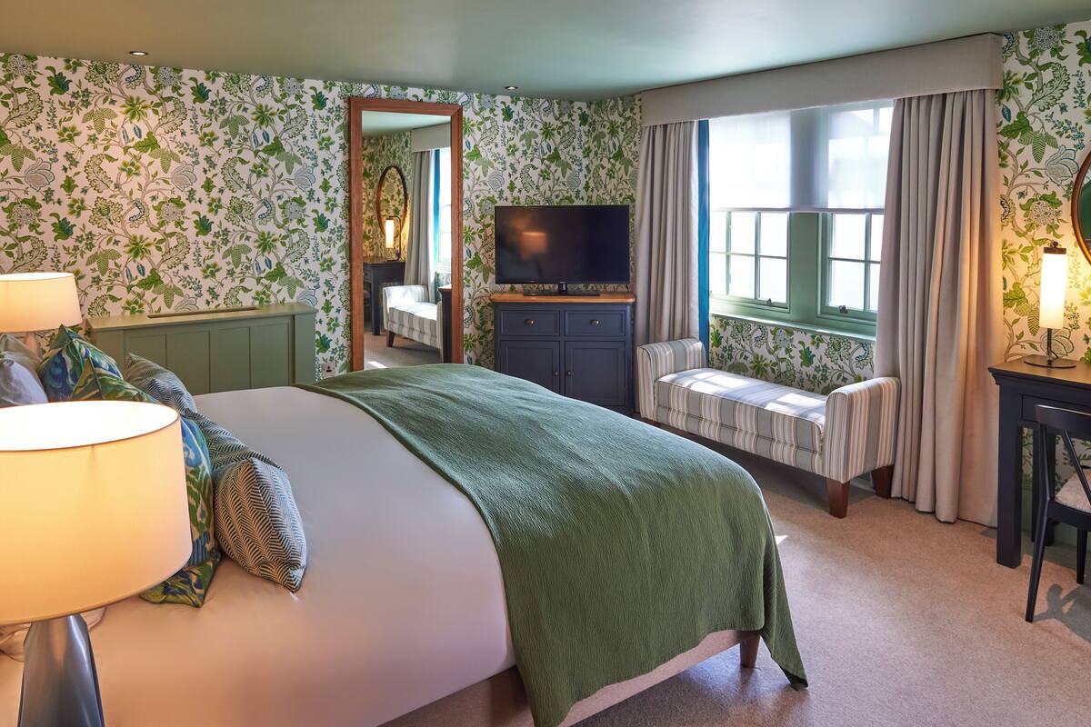 A hotel room with a bed, a TV, a bench, and a window with curtains.