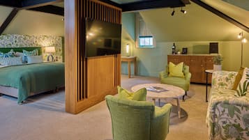 Ein Schlafzimmer mit Bett, Fernseher und Nachttisch. Es gibt eine Sitzecke mit Sofa, Couchtisch und Lampe. Der Raum hat Holzbalken an der Decke und ein Fenster mit Blick nach draußen.