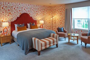 Ein Hotelzimmer mit einem großen Bett, zwei Sesseln, einem kleinen Tisch und einem Fenster mit Blick.