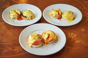 Tres platos de huevos benedictinos sobre una mesa de madera.