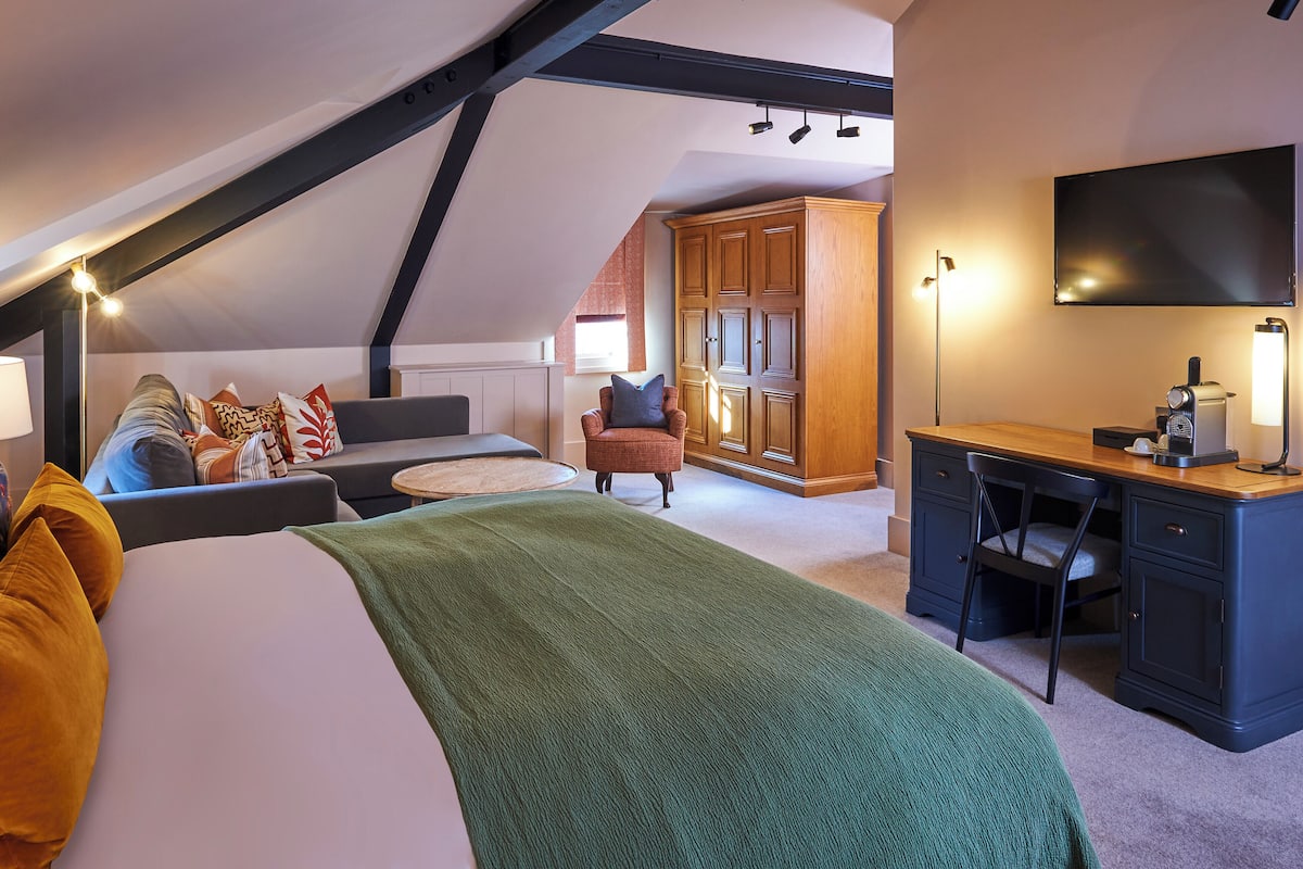 A cozy bedroom with a bed, a desk, and a chair. There is a wardrobe and a television.