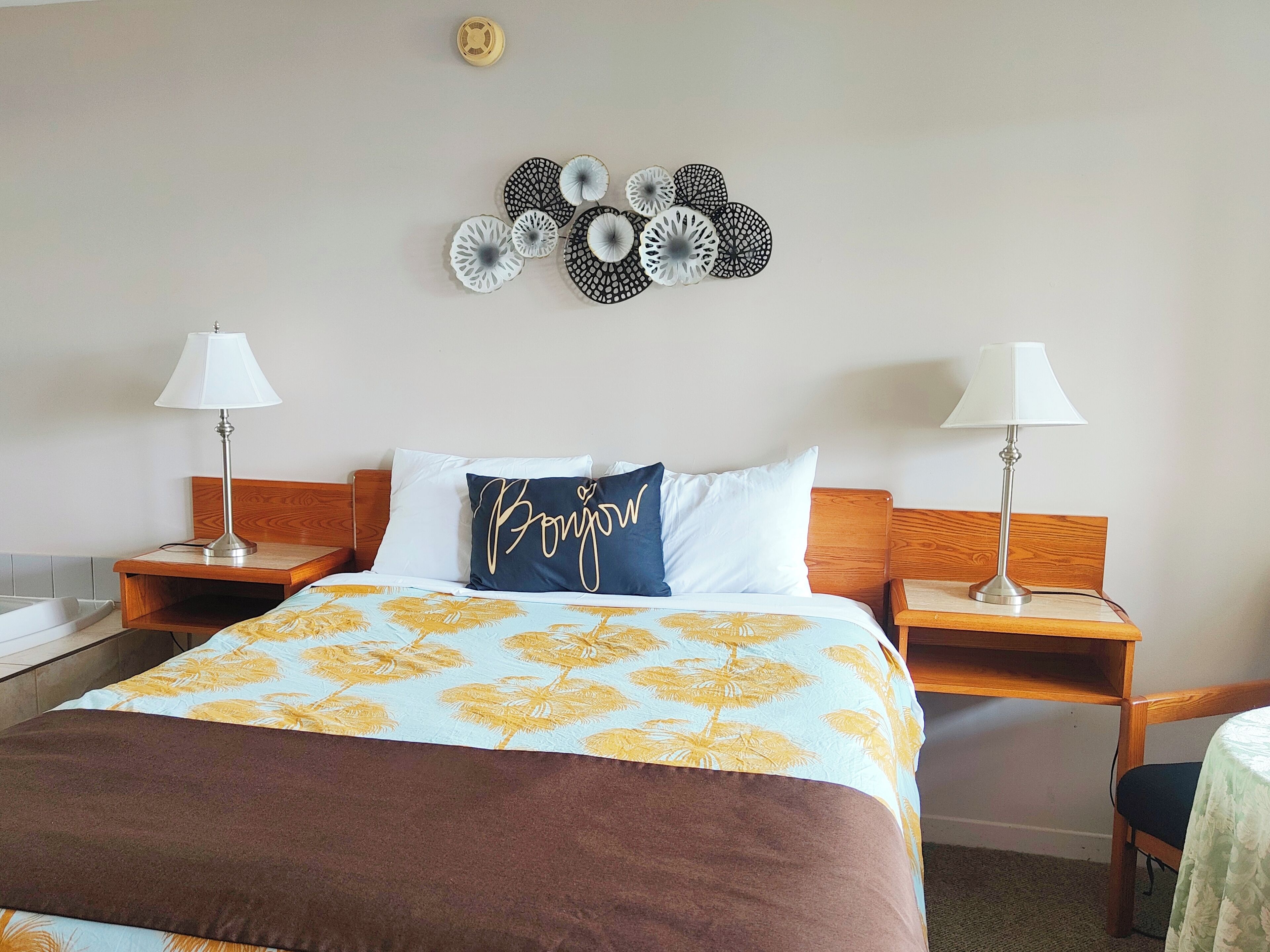 Een net opgemaakt bed met een bloemenbedekking, twee bedlampjes, een houten hoofdbord en een wanddecoratie erboven.