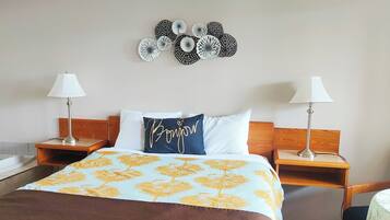 Een net opgemaakt bed met een bloemenbedekking, twee bedlampjes, een houten hoofdbord en een wanddecoratie erboven.