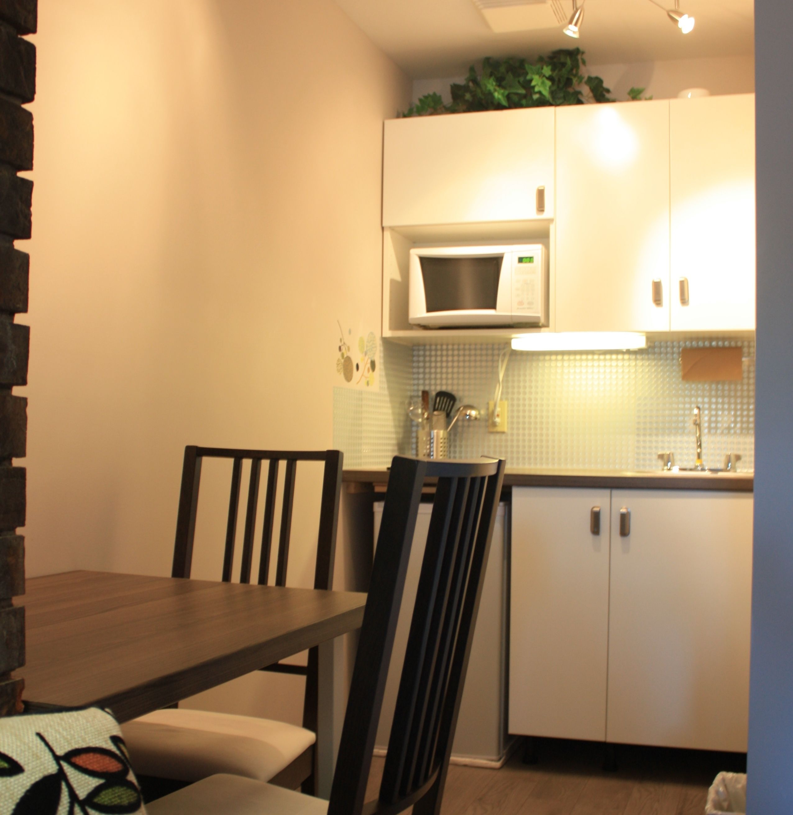 A compact kitchen with white cabinets, a microwave, and a sink. There is a dining table with chairs.