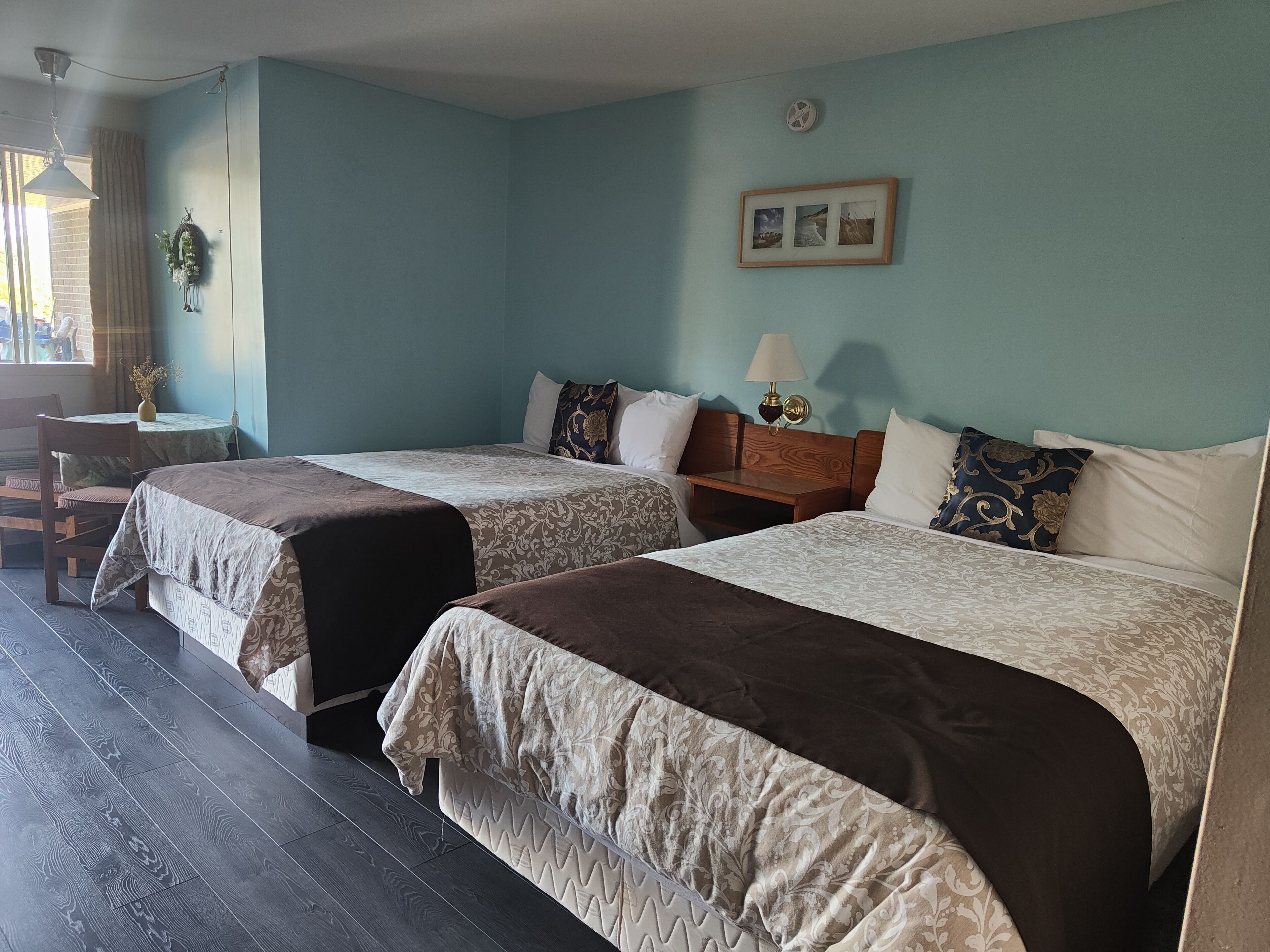 A hotel room with two beds, a small table, a chair, and a window with curtains.