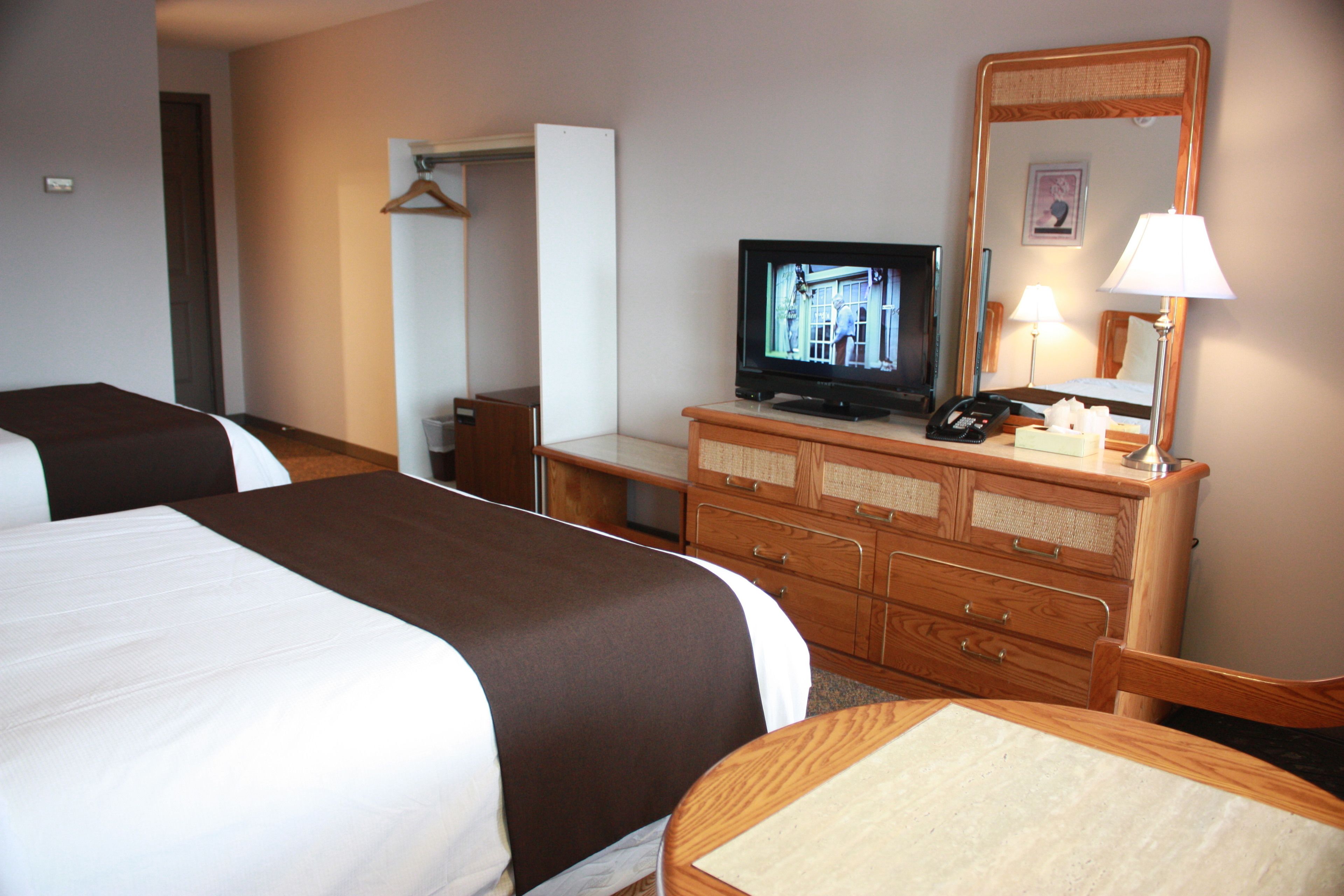A hotel room with two beds, a television, a dresser, and a mirror.