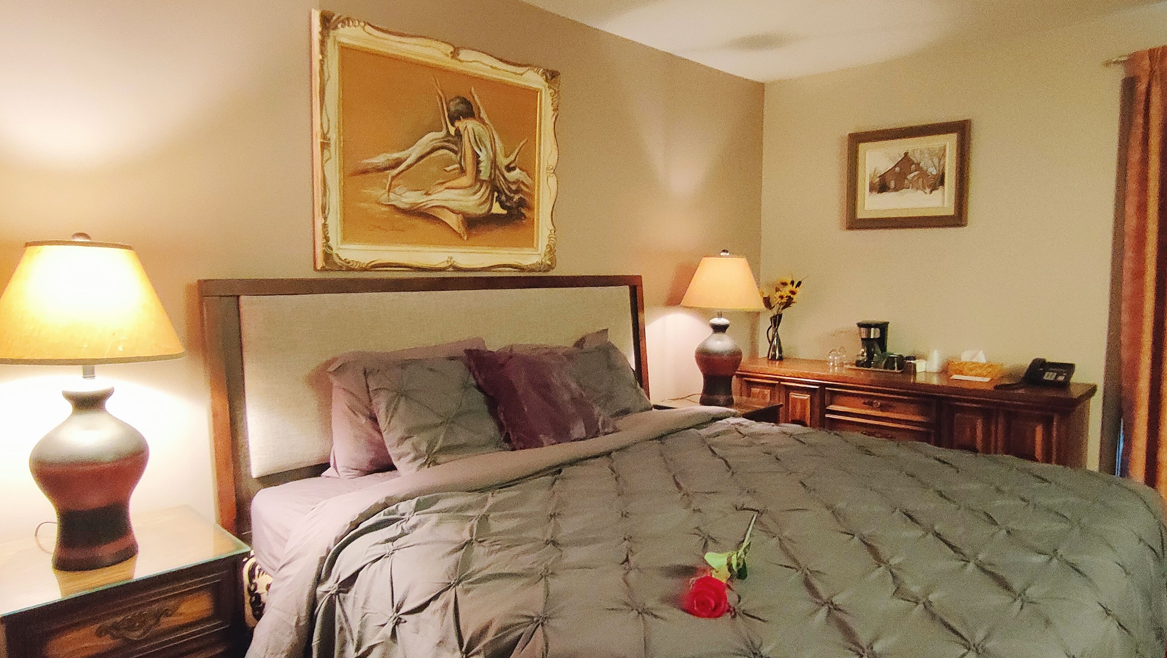 A hotel room with a large bed, two bedside lamps, a nightstand, a dresser, and a framed picture on the wall.