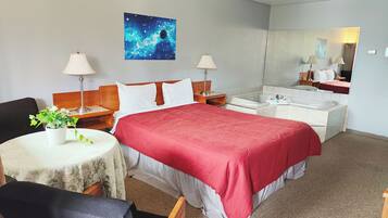 Habitación de hotel con cama, dos mesitas de noche, una silla, una mesita pequeña con una planta, un espejo y un cuadro de una galaxia.