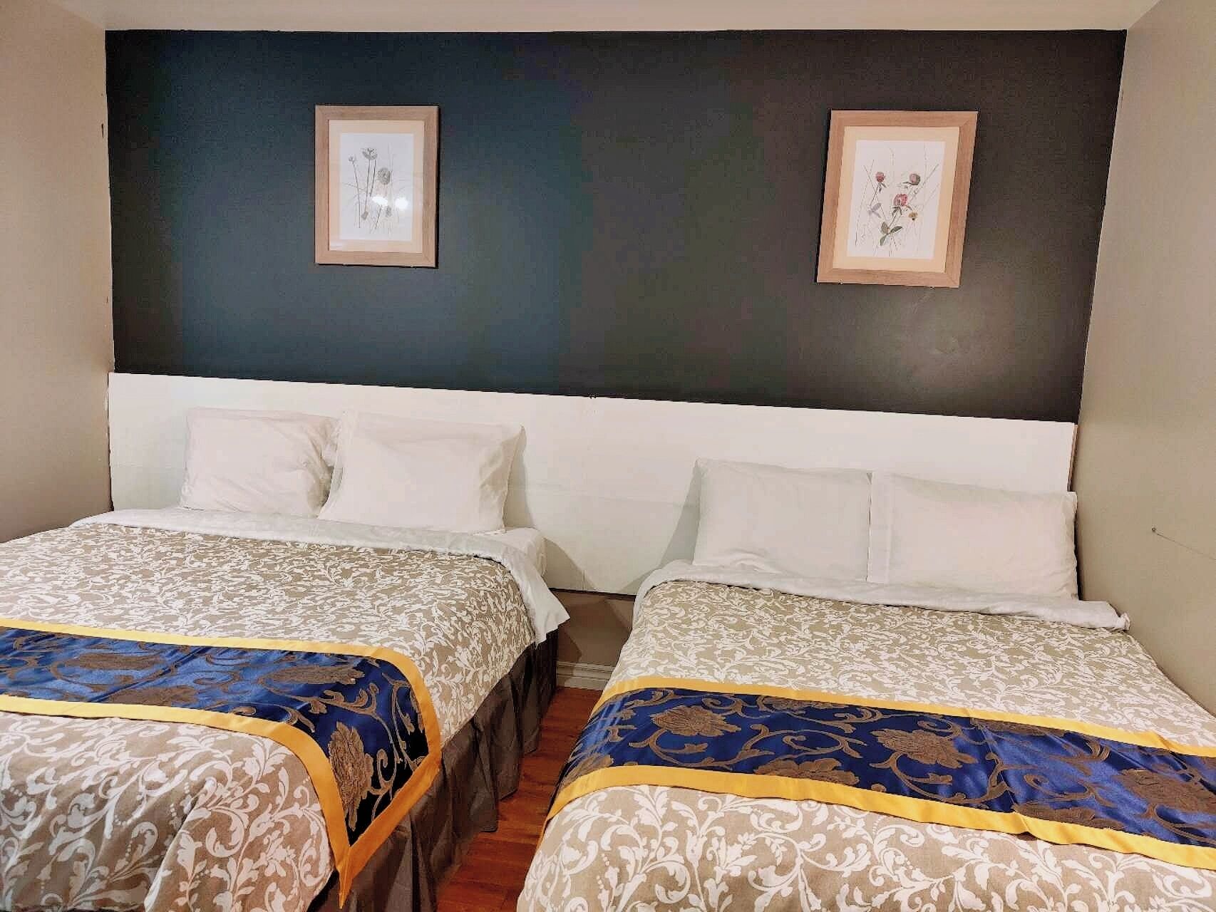 A hotel room with two beds, each with a patterned bedspread and matching pillows. There are two framed pictures on the wall above the beds.