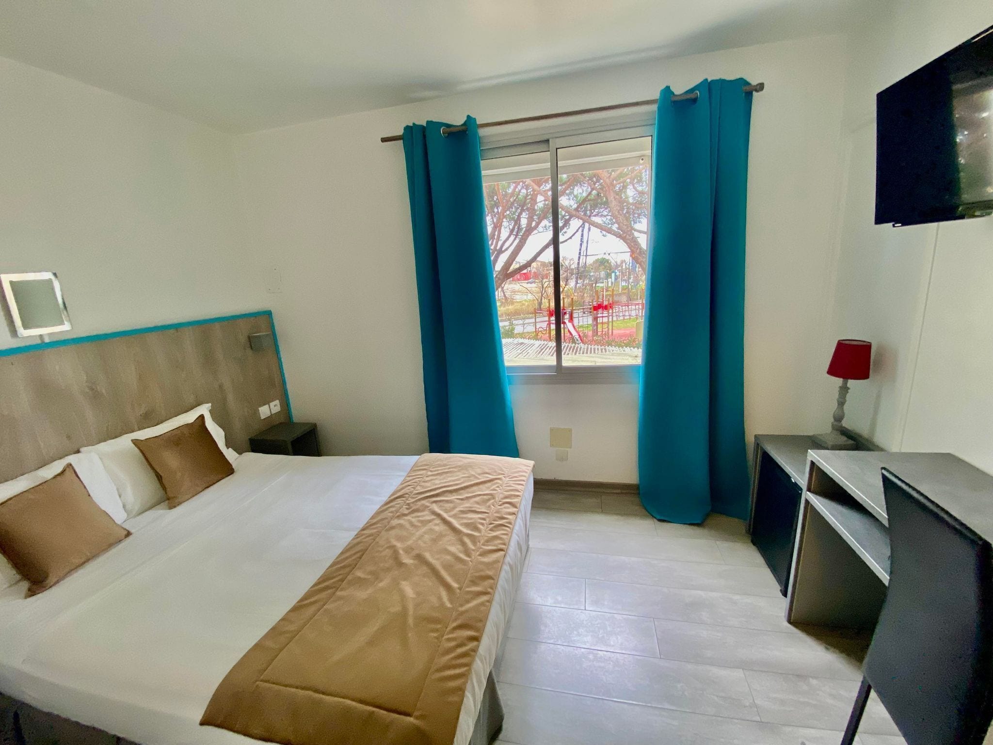 Ein Hotelzimmer mit Bett, Schreibtisch, Fernseher und einem Fenster mit Vorhängen.