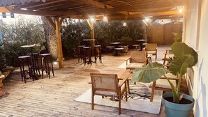 Une terrasse extérieure avec des tables et des chaises en bois, des guirlandes lumineuses et des plantes en pot.