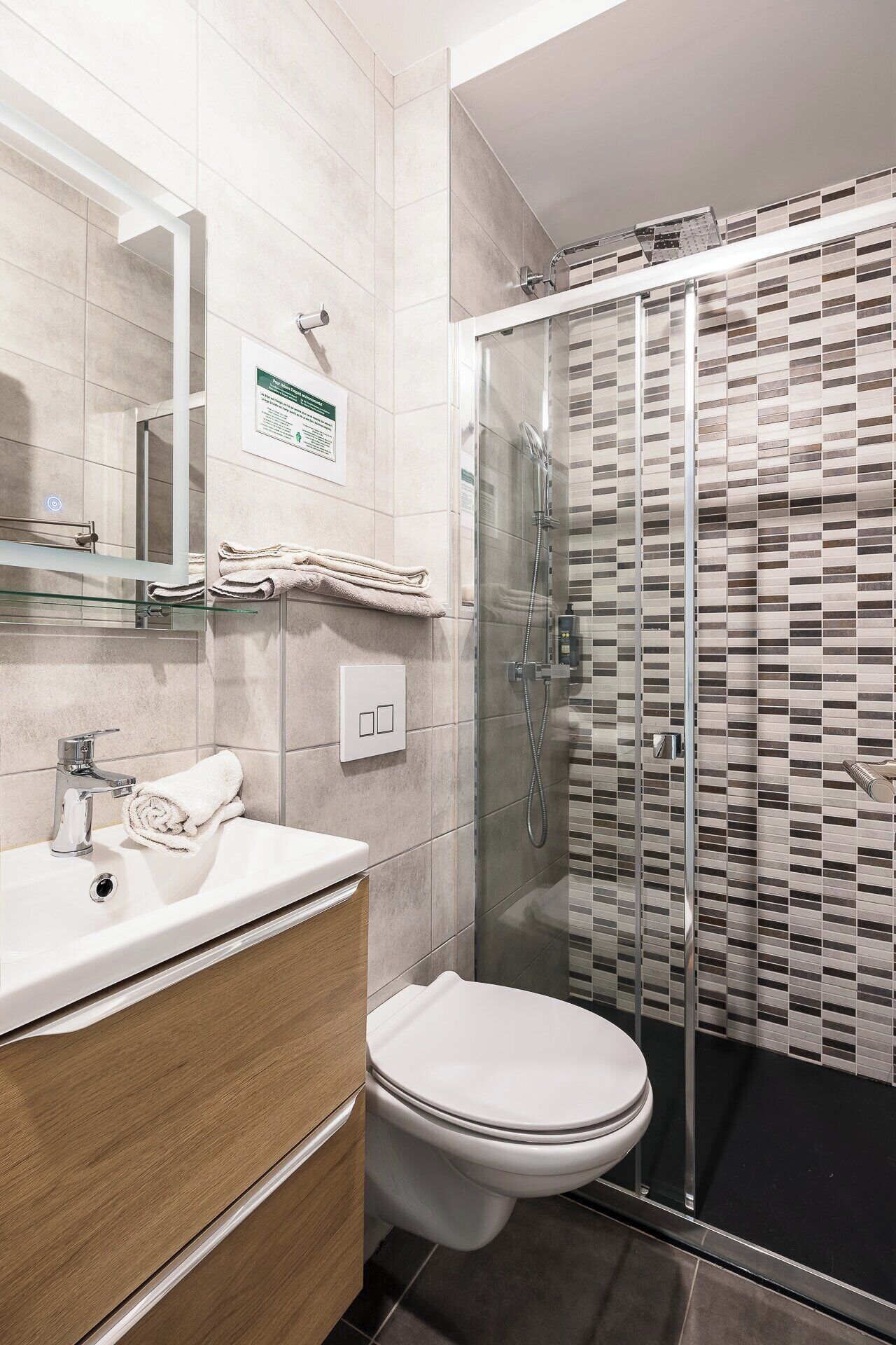 Un baño moderno con cabina de ducha de vidrio, lavamanos blanco y un inodoro.