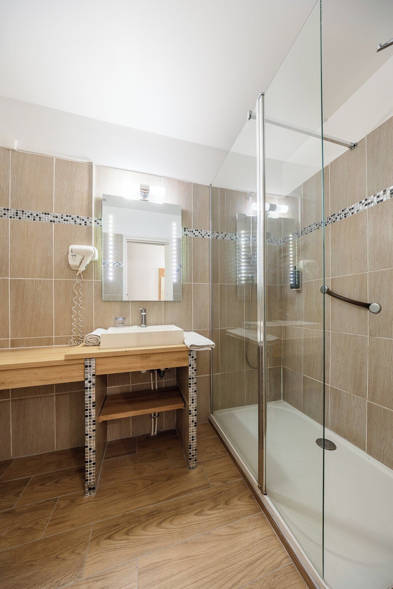 Un baño moderno con tocador de madera, cabina de ducha con mampara de vidrio y suelo de baldosas.