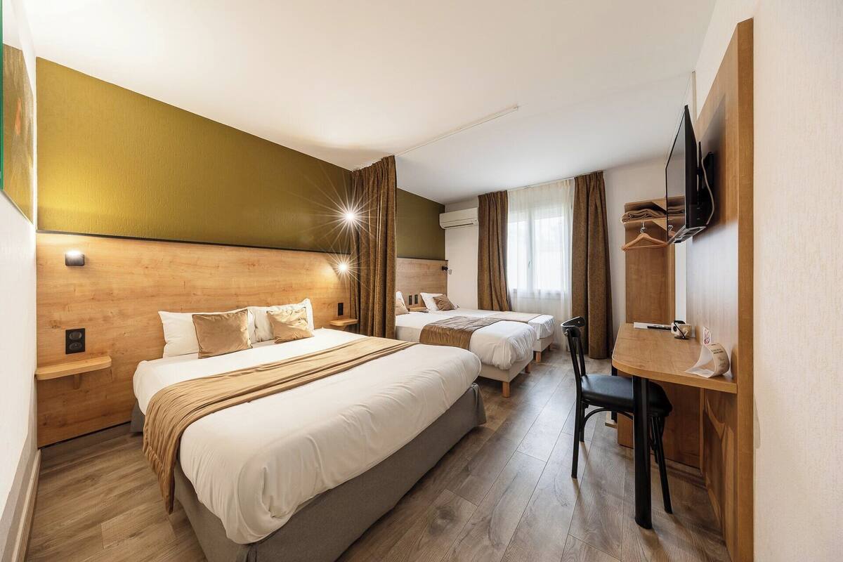 A hotel room with two beds, a desk, a chair, a TV, and a window with curtains.