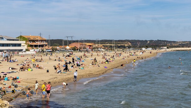 Une plage bondée où les gens se prélassent au soleil et se baignent.