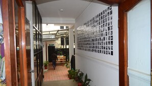 A hallway with a tiled floor, potted plants, and a wall with a grid of photographs. - Holy Lodge (Kathmandu)