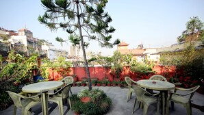An outdoor patio with a round table and chairs, surrounded by potted plants and a tree. - Holy Lodge (Kathmandu)