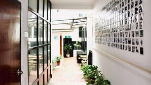 A corridor with a tiled floor, potted plants, a wall with a grid of black and white photos, and a door on the left. - Holy Lodge (Kathmandu)