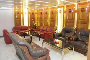 A spacious living room with leather sofas, a glass coffee table, and wooden doors with decorative carvings. - Hotel Sweet Dream (Dhaka)