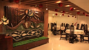 A dining area with a large wooden mural, multiple tables, and chairs. - Hotel Sweet Dream (Dhaka)