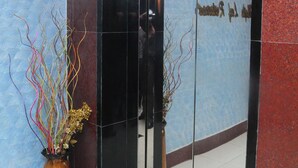 A reception area with a glass door, a vase with decorative branches, and a patterned wall. - Hotel Sweet Dream (Dhaka)