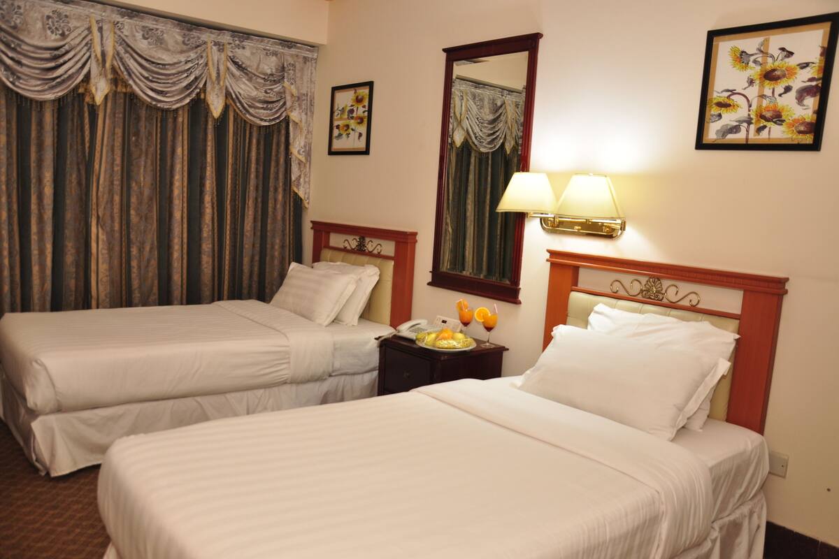 A hotel room with two beds, a nightstand with a lamp, a mirror, and a framed floral artwork on the wall.