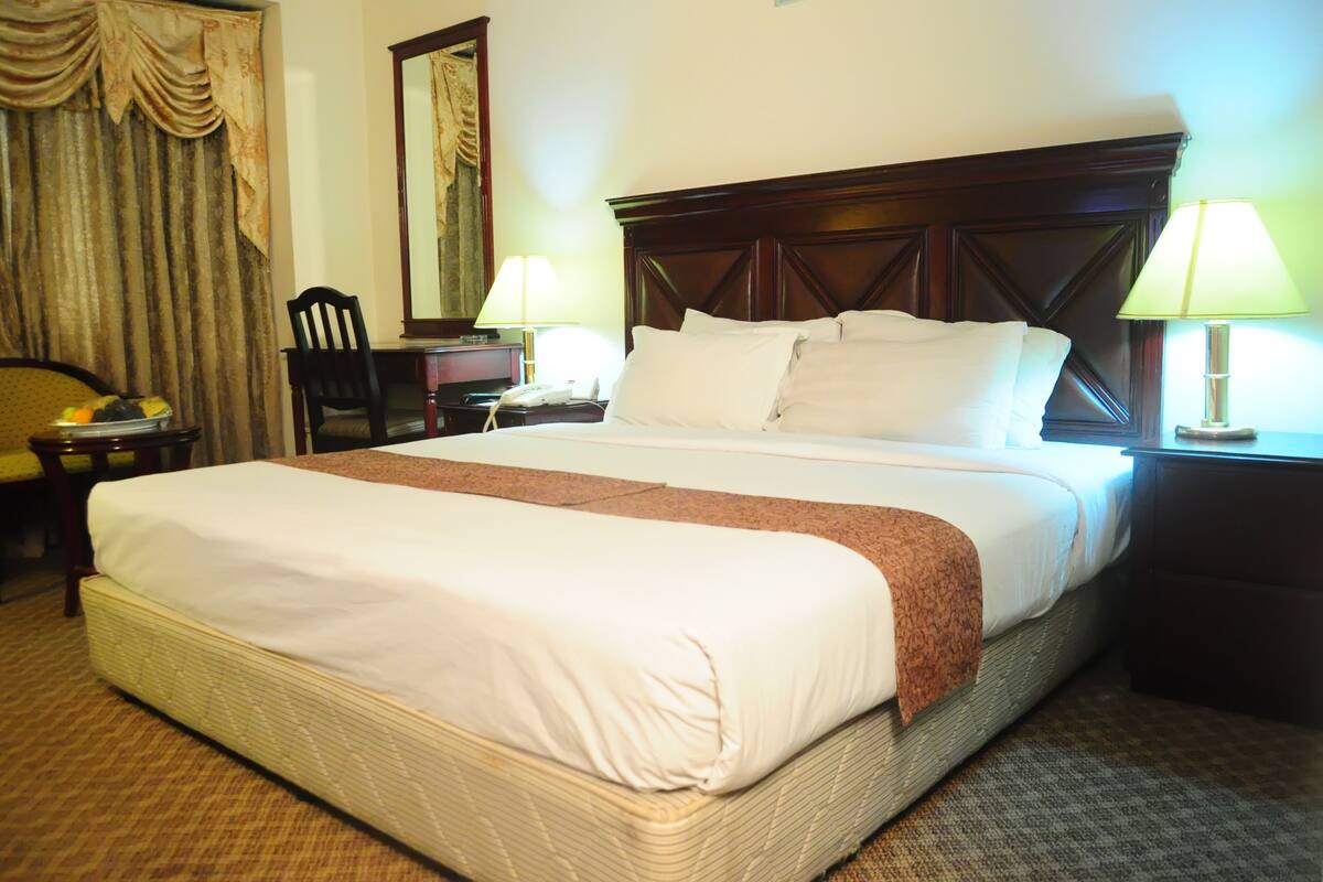 A hotel room with a large bed, two bedside tables with lamps, a chair, a desk, and a mirror on the wall.
