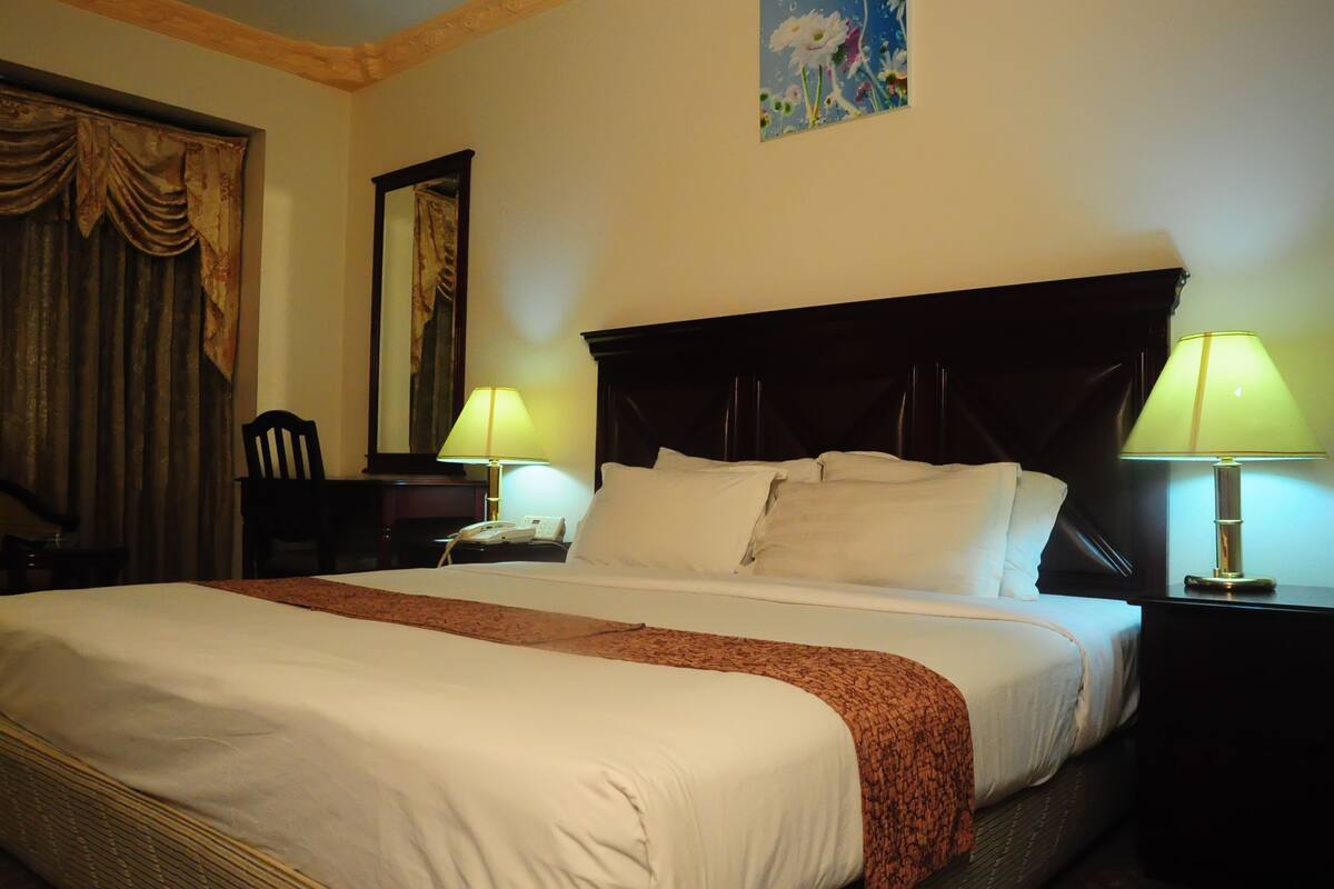 A hotel room with a large bed, two bedside lamps, a nightstand, a chair, and a painting on the wall.