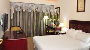 A hotel room with a large bed, a desk with a telephone, a chair, a lamp, and a window with curtains. - Hotel Sweet Dream (Dhaka)
