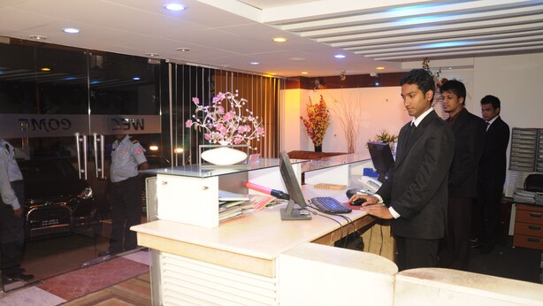 A reception desk with a computer, a vase of flowers, and a car parked outside. - Hotel Sweet Dream (Dhaka)