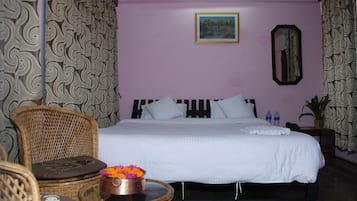 A hotel room with a bed, a wicker chair, a small table with a flower vase, a mirror, and a picture on the wall.