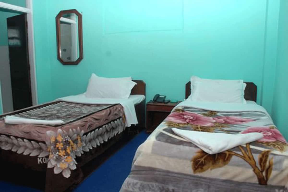 A room with two beds, each with a different floral bedspread, a small bedside table with a lamp, and a mirror on the wall.